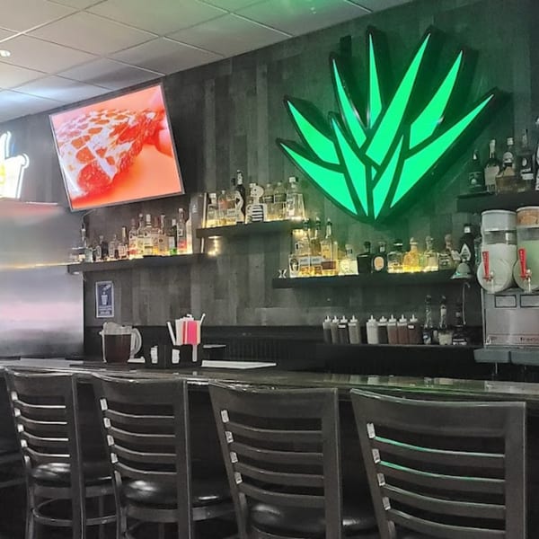 Casa Agave Mexican Cuisine bar with a glowing green agave sign, liquor bottles, and bar stools.