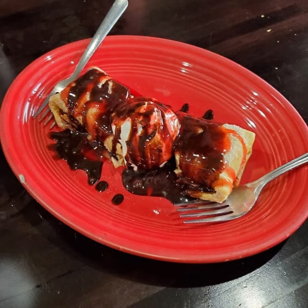 Two chimichangas topped with vanilla ice cream, chocolate, and strawberry syrup on a red plate.