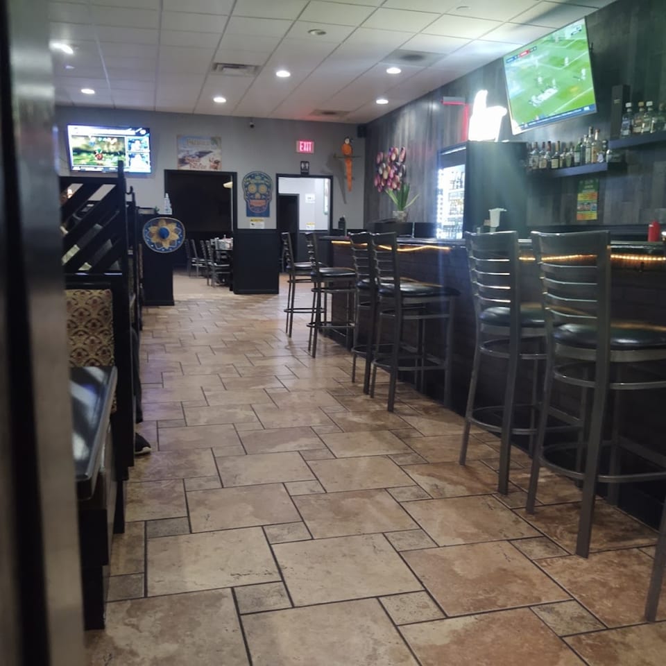 Interior of Casa Agave Mexican Cuisine, showing a bar with stools, dining booths, and TVs.