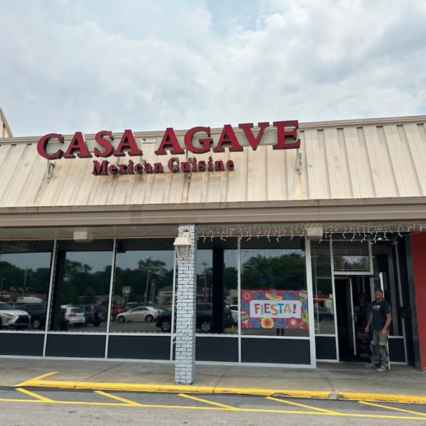 Exterior of Casa Agave Mexican Cuisine restaurant with a red sign and a person standing in the doorway.