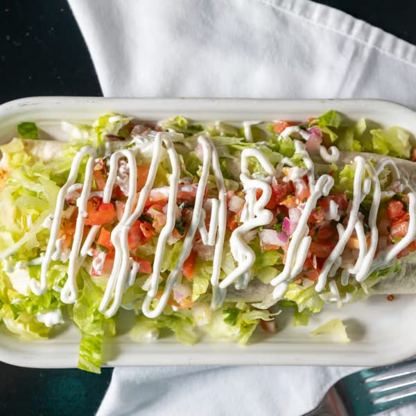 A large burrito topped with shredded lettuce, pico de gallo, and a drizzle of sour cream.